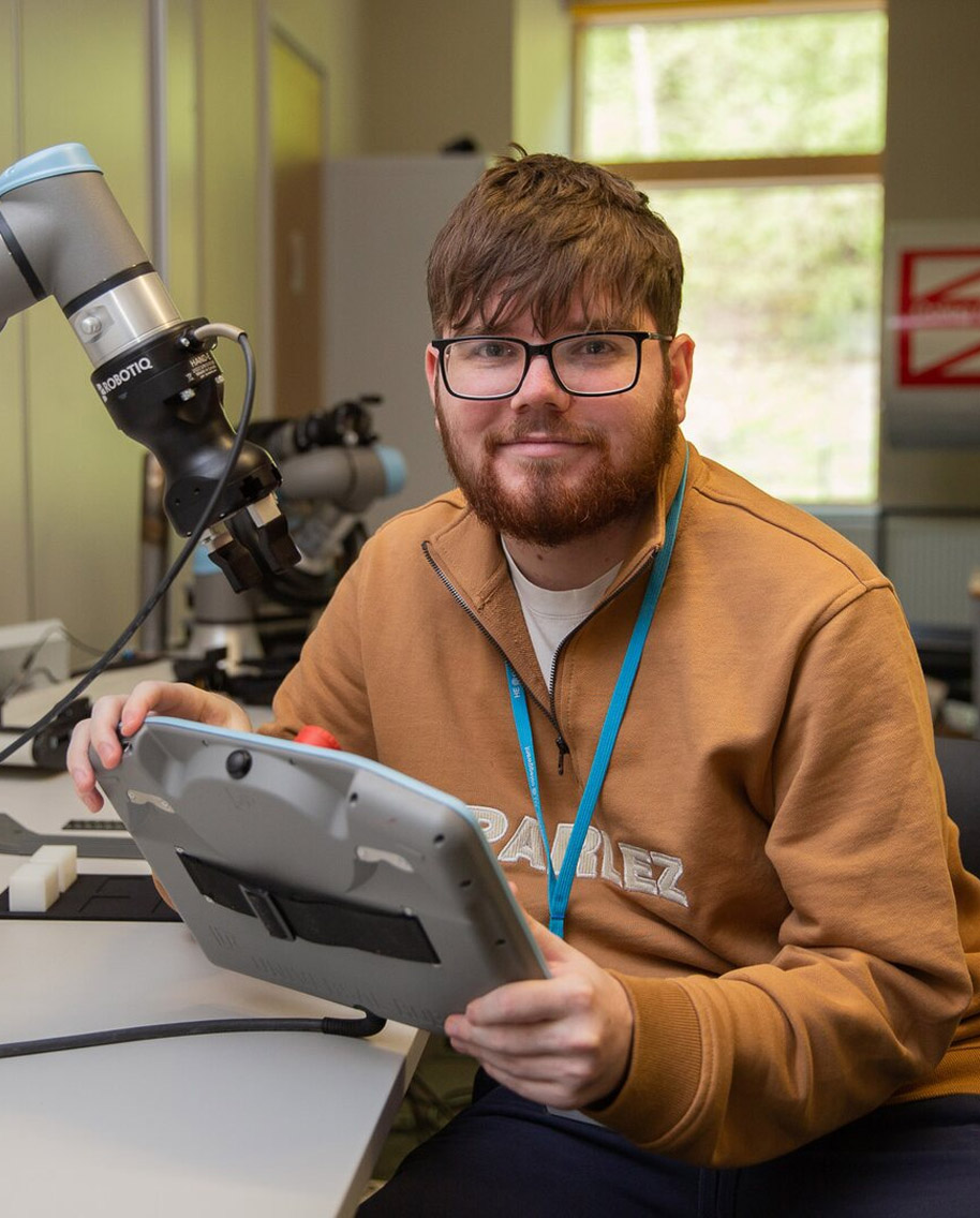 Student holding tablet next to a robotic arm