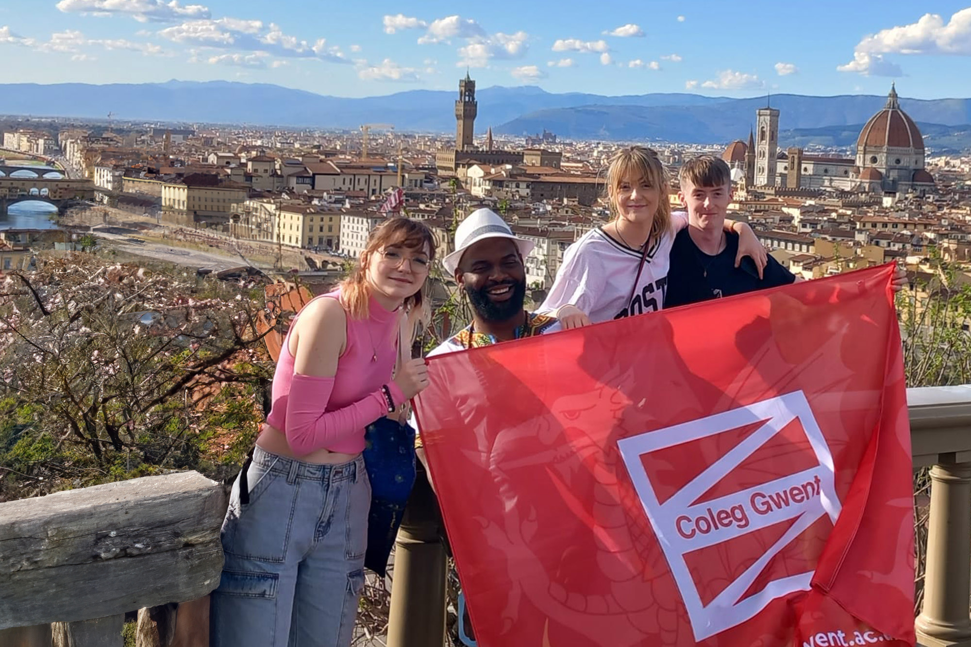 Students smiling holding a Coleg Gwent flag in Italy