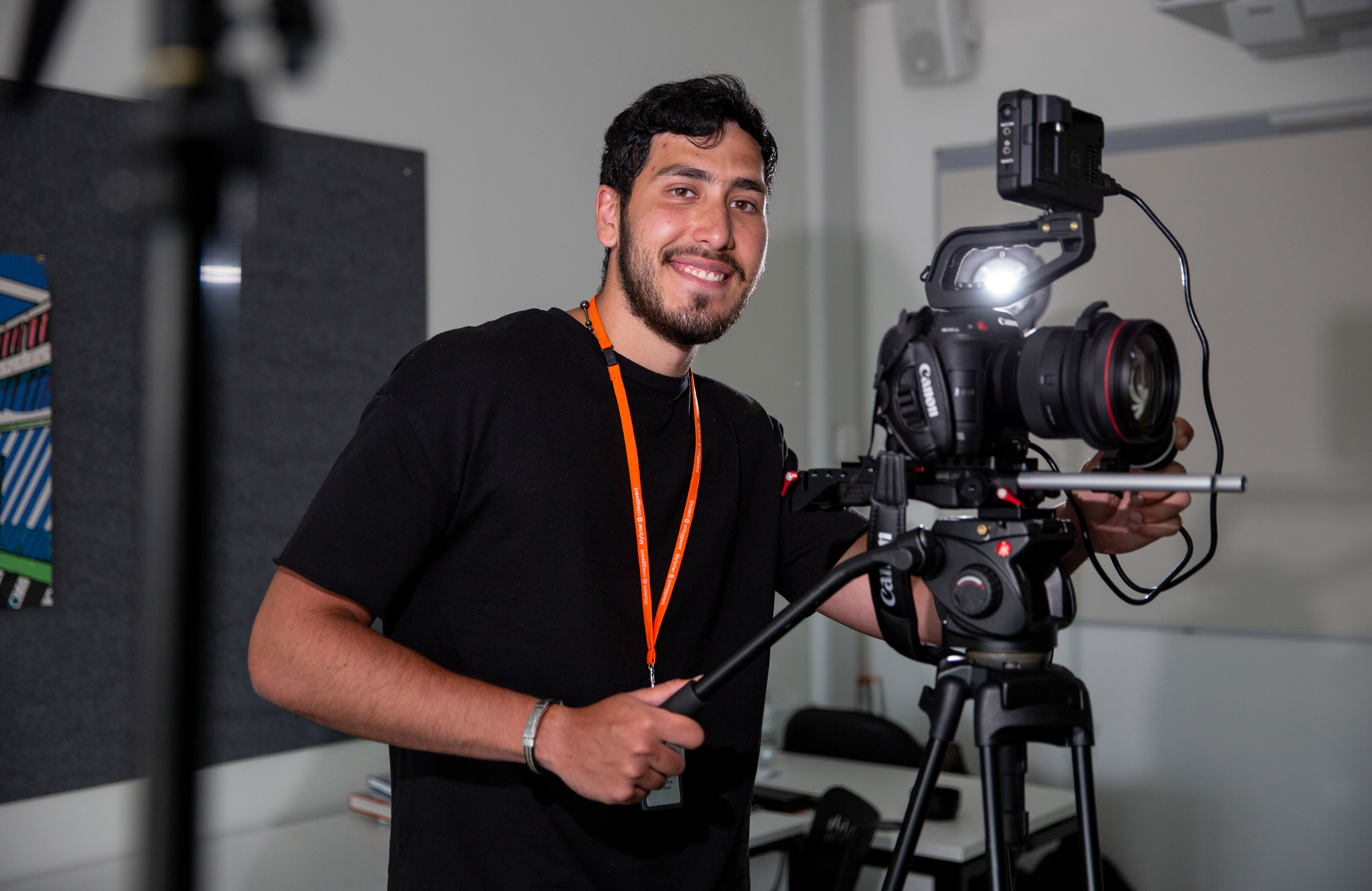 Media student smiling with hands on video camera
