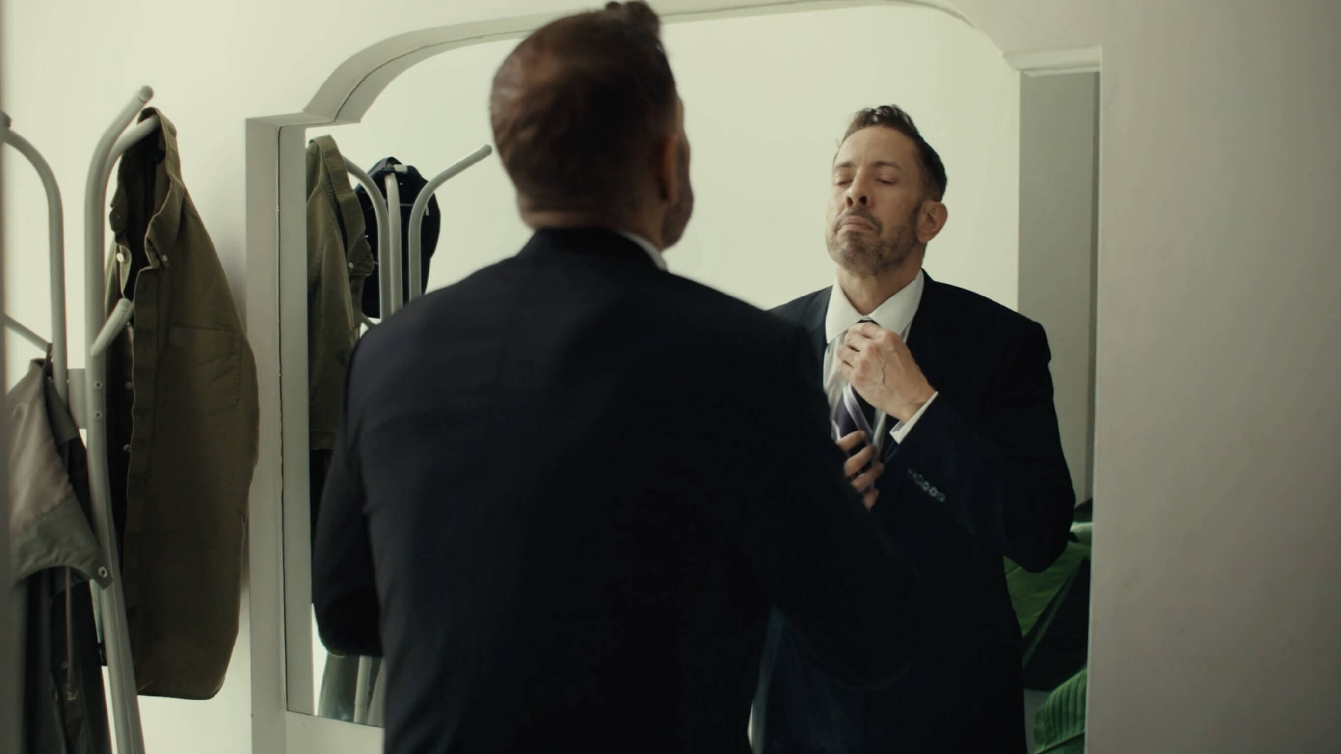 Man in suit looking in mirror doing tie